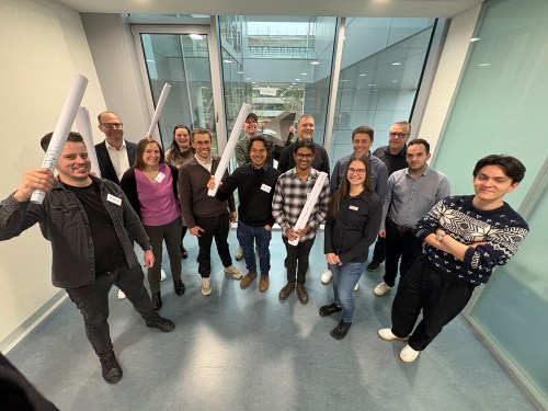 Group of people standing in a modern office space, holding rolled-up papers, participating in the kick-off meeting for the 'FunkBau' Network at TU Darmstadt.